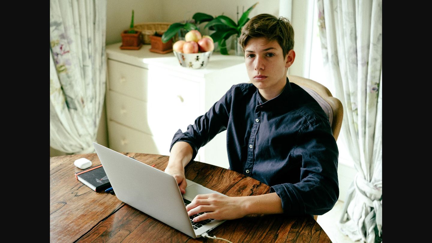 Teenage student learning comfortably at home using laptop at kitchen table, demonstrating family-centred online education in a warm domestic environment